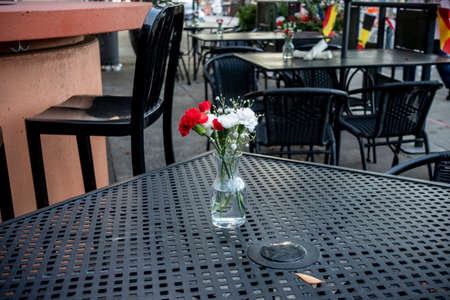 Side view of a glass vase filled with red and white carnations, on top of a black table in the outdoor seating area of a restaurantの写真素材