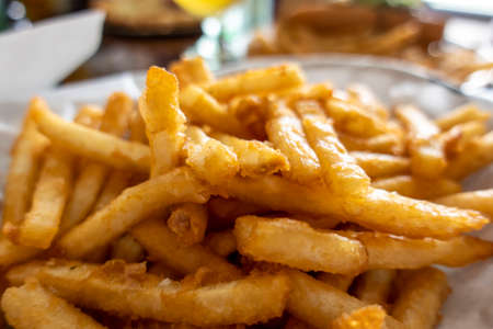 Close up view of battered and fried, golden french fries in a basket lined with white paper at a restaurant tableの写真素材