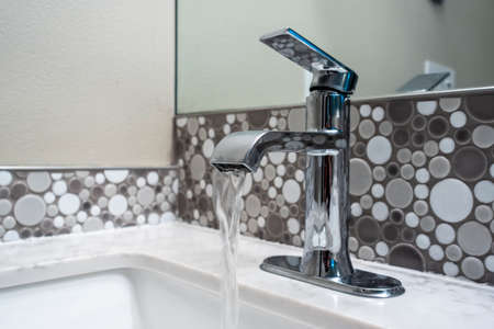 Close up view of a sink faucet inside an upscale bathroom, the water currently running from the tap