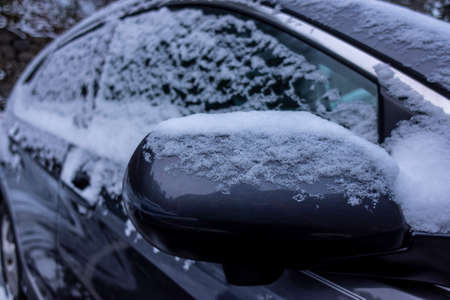 Selective focus on an icy, snow covered car rear view mirror during a snowstorm in the pacific...