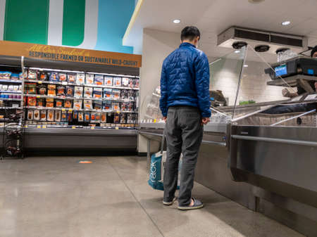 Kirkland, WA USA - circa February 2022: View of an Asian man in a blue jacket ordering fresh seafood...
