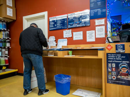 Kirkland, WA USA - circa December 2021: Angled view of a person shipping a package at a USPS during...