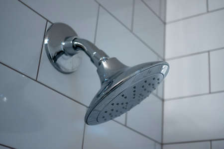 Selective, macro focus on a silver shower head inside a white tiled bathroomの写真素材