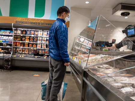 Kirkland, WA USA - circa February 2022: View of an Asian man in a blue jacket ordering fresh seafood...