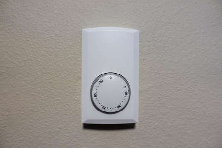 Close up view of a white air cooling and heating control panel on an off white colored wall inside a houseの写真素材