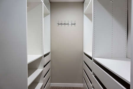 View of tall, white cabinets and drawers inside a narrow walk in closet inside a master bedroomの写真素材