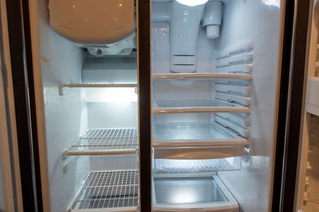 View of a white, empty fridge with the door wide open to see several shelves and drawers devoid of...