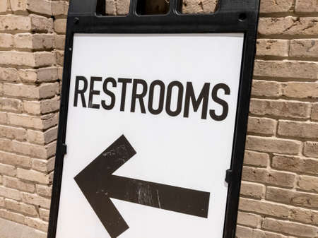 Angled view of a sandwich board pointing the direction of public restrooms, leaning against a brick wallの写真素材