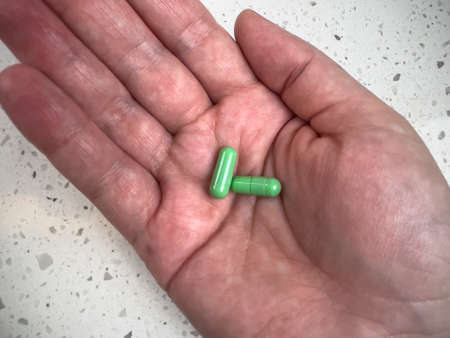 Close up view of two green pills in the palm of an adult hand, shot against a light background