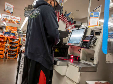 Kirkland, WA USA - circa September 2021: Angled view of a man wearing a face mask checking out at a self checkout kiosk inside a QFC grocery store.のeditorial素材
