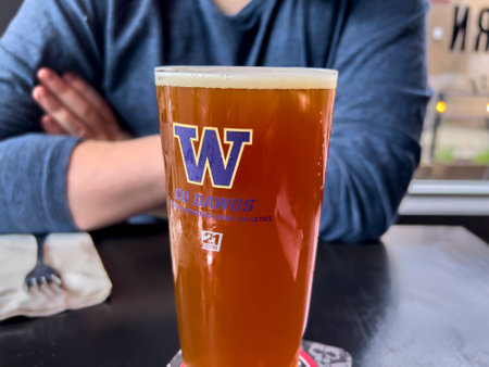 Seattle, WA USA - circa June 2022: Close up view of a frothy beer in a University of Washington glass inside a local bar.のeditorial素材