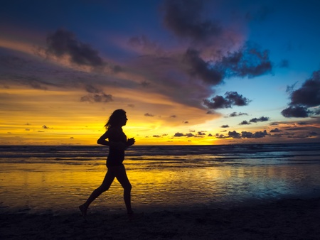 A silhouetted view of slim girl running for marathon on the beach under beautiful sunsetの写真素材