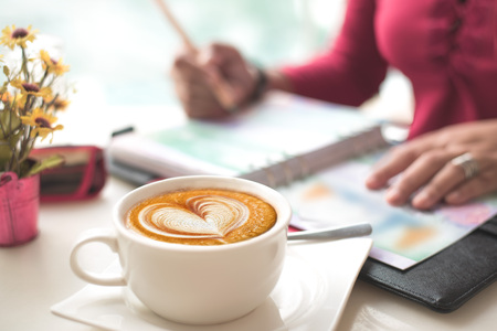 Coffee with Heart Shape Latte Art on Working Desk. Moody Shot, blur working   woman checking figure in her chart in books. Concept passion work.の写真素材
