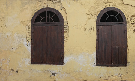 Old Wooden Half Circle Arched Windows. Dark Wood Half Moon Windows with Cream Pastel Yellow Color Damage Aged Brick Wallの写真素材
