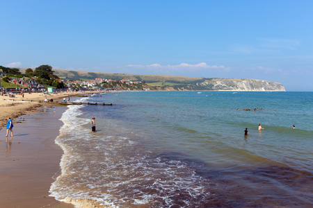 Bathers in the sea Swanage beach Dorset England UK with waves on the shore near Poole and Bournemouth at the eastern end of the Jurassic Coast a World Heritage Site popular south coast tourist destinationのeditorial素材