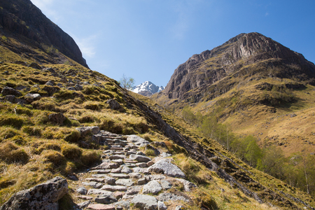 Path up to Glencoe snow topped mountains Scotland UK in Scottish Highlands in spring with blue sky and sunshineの写真素材