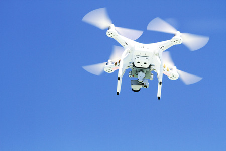 White drone  flying with camera record liens against blue sky