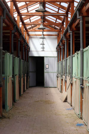 Inside modern clear stable or barn with horse boxes. Passageway view in natural light in the end. Cleared empty stall in the stable keeping sport horsesの写真素材