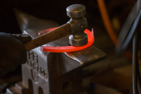 Hard work in the smithy on the anvil. Hammering glowing steel horse shoe. Blacksmith forges a hot horseshoeの写真素材