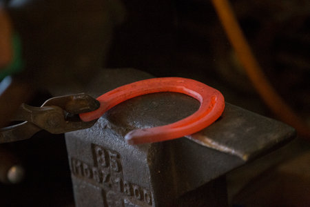 Hard work in the smithy on the anvil. Hammering glowing steel horse shoe. Blacksmith forges a hot horseshoeの写真素材