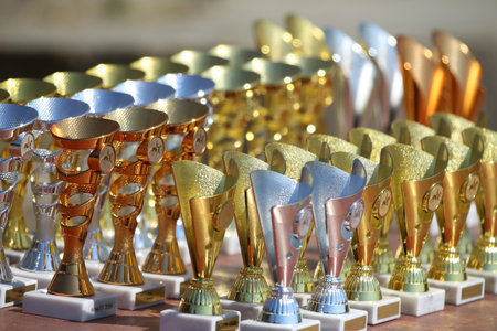 Award trophies waiting for competitors after amateur equestrian championship in row. Golden silver and bronze prizes for winners at an outdoor sport event. Colorful sport trophy backgroundの写真素材