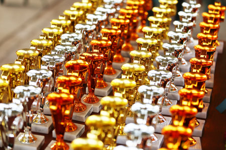 Award trophies waiting for competitors after amateur equestrian championship in row. Golden silver and bronze prizes for winners at an outdoor sport event. Colorful sport trophy backgroundの写真素材