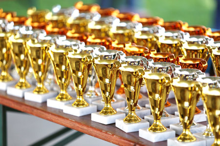 Award trophies waiting for competitors after amateur equestrian championship in row. Golden silver and bronze prizes for winners at an outdoor sport event. Colorful sport trophy backgroundの写真素材