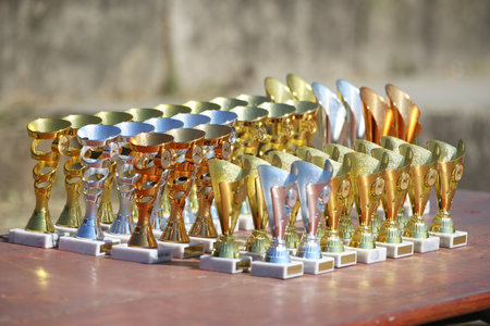 Award trophies waiting for competitors after amateur equestrian championship in row. Golden silver and bronze prizes for winners at an outdoor sport event. Colorful sport trophy backgroundの写真素材
