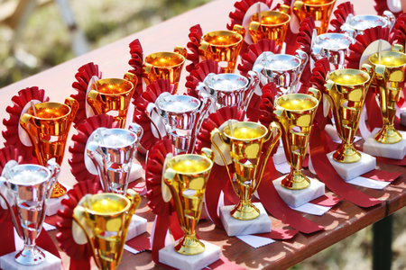 Award trophies waiting for competitors after amateur equestrian championship in row. Golden silver and bronze prizes for winners at an outdoor sport event. Colorful sport trophy backgroundの写真素材