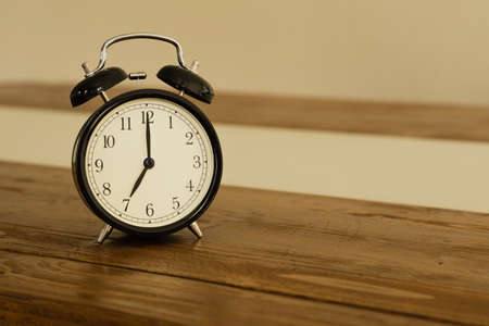 Vintage alarm clock on rustic wood table. Shows 7 o'clock.