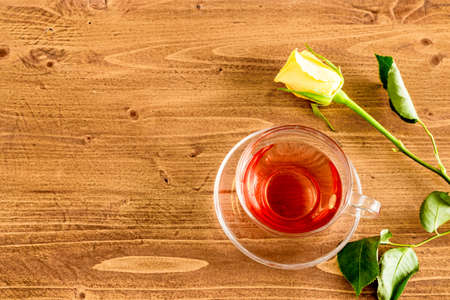 Yellow rose and a cup of black tea in a transparent glass cup on rustic wooden table top. Top view. Flat.の写真素材
