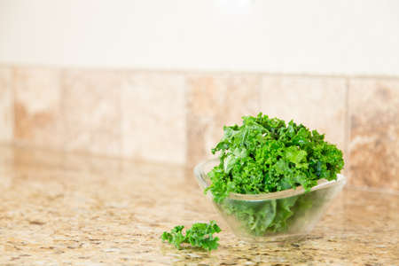 A bowl of fresh green kale in a glass bowl on a granite countertop. Copy space.の写真素材