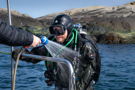 April 17, 2021 - Hamburgsund, Sweden: A scuba diver have just return to the dive boat and shower off the salt from his equipment.のeditorial素材