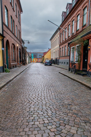 An empty narrow cobblestone street with old colorful buildings with brick walls in light rain....