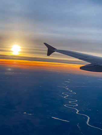 A picture from an airplane of a sunset. View from the window with the wing visible. Traveling in...