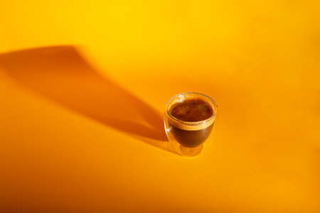 Freshly brewed creamy espresso in a glass coffee cup isolated on yellow background, close up with copy spaceの写真素材
