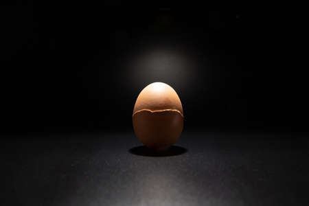Broken chicken eggshell isolated on black background with copy space. Light filters through the cracks.の写真素材
