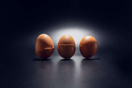 Three broken chicken eggshells in line isolated on black background with copy space. Light filters through the cracks.の写真素材