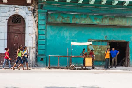 Havana / Cuba - 04.15.2015: Three Cuban women walking in front of a work place where two Cuban men are standing and talking, two kids playing on an old stallのeditorial素材