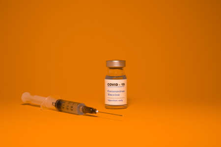 Vaccine bottle (phial) with a label that reads "Covid - 19 Corona virus Vaccine injection only" & a medical syringe isolated on orange Vaccination for prevention, immunization & treatment to virusの写真素材