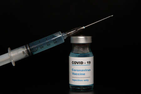 Small vaccine bottle (phial) with a label that read "Covid - 19 Corona virus Vaccine injection only" & a medical syringe isolated on black Vaccination for prevention, immunization & treatment to virusの写真素材