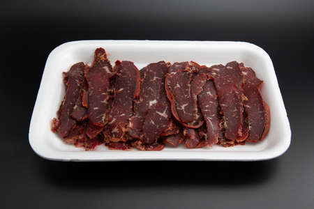 Turkish traditional pastirma (pastrami) in a white  container isolated on black background with copy...