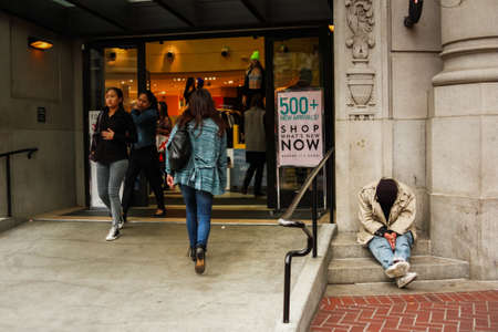 San Francisco, California / United States of America - May 27th 2013: Homeless man sitting outside a luxury shopping mall as people walk by, San Francisco, California, United States of America aka USAのeditorial素材
