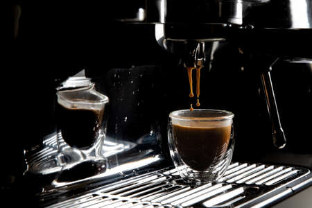 Dark coffee drops dripping in a transparent glass espresso cup on a manual espresso machine with copy space, close upの写真素材