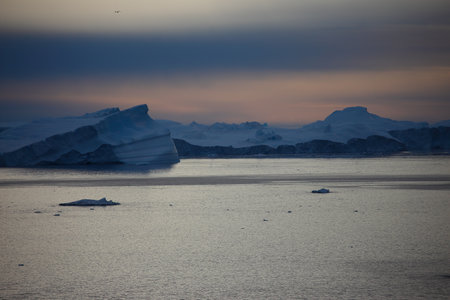Antarctic landscape with icebergs and ice floats at sunset.