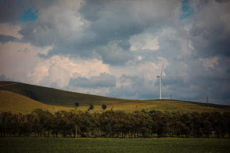 Wind turbines in a field with trees under a stormy sky.の写真素材
