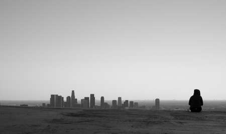 Single silhoutted seated figure next to skyline of downtown Los Angelesの写真素材