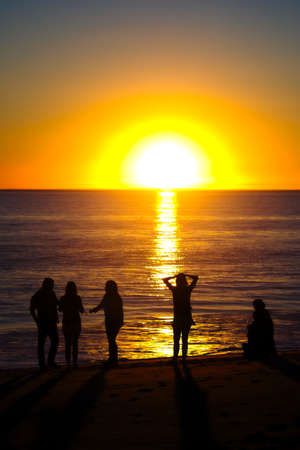 Family on the beach silhouetted by setting sunの写真素材