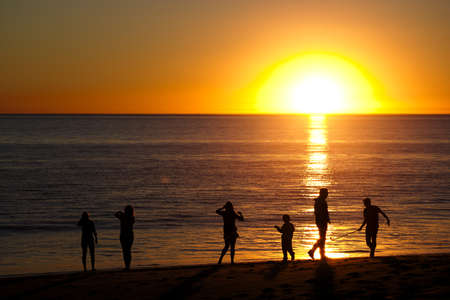 Family playing on beach and silhouetted by sunsetの写真素材