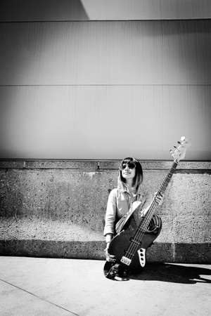 Woman holding guitar while crouched on groundの写真素材